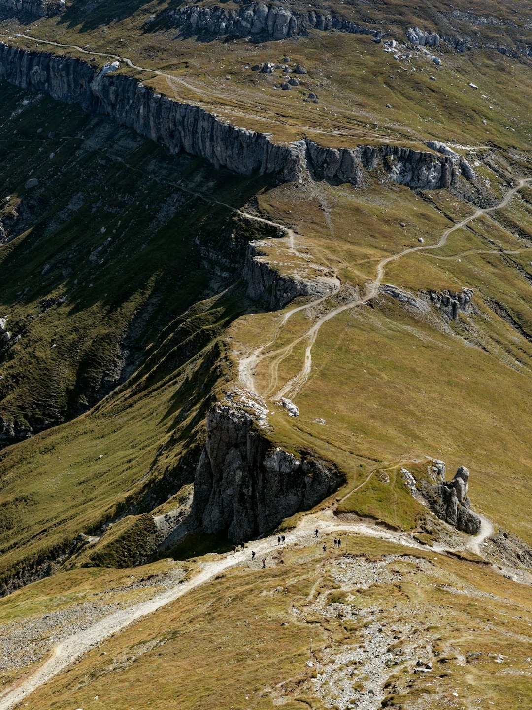 Hikers walk along a winding dirt path on a mountain ridge.