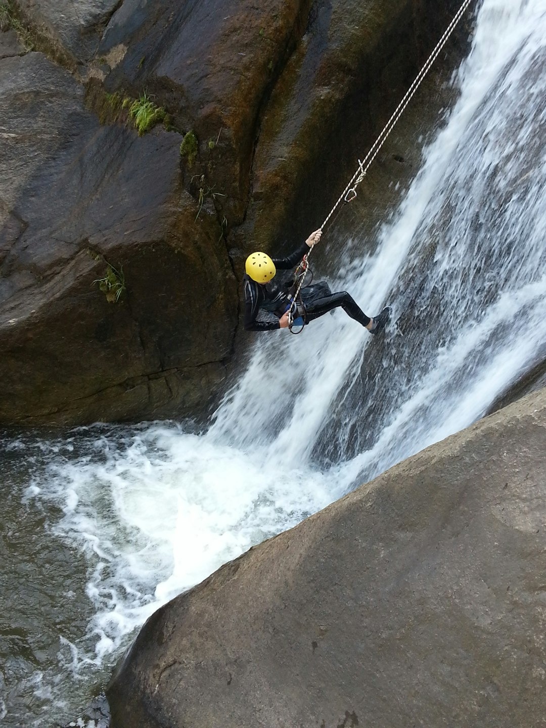 A person in a wetsuit rappels down a rocky waterfall.